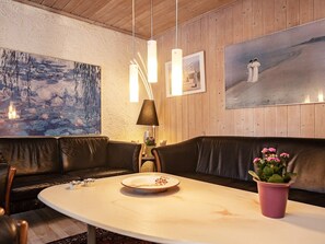 A room with a wooden wall, a painting, a sofa, a table with a plate, and a lamp.