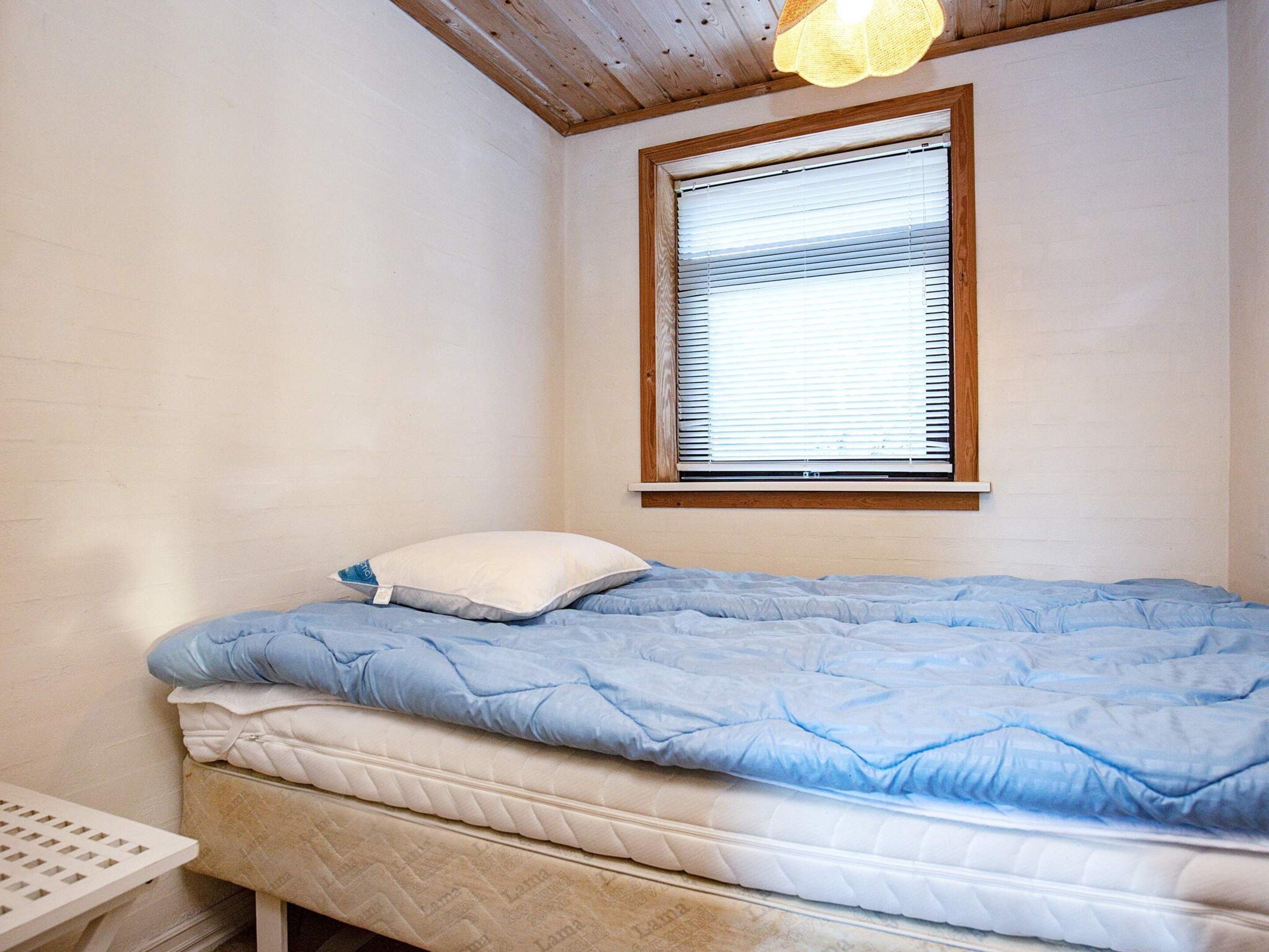 Une chambre à coucher avec un lit, une fenêtre avec des stores et un luminaire au plafond.