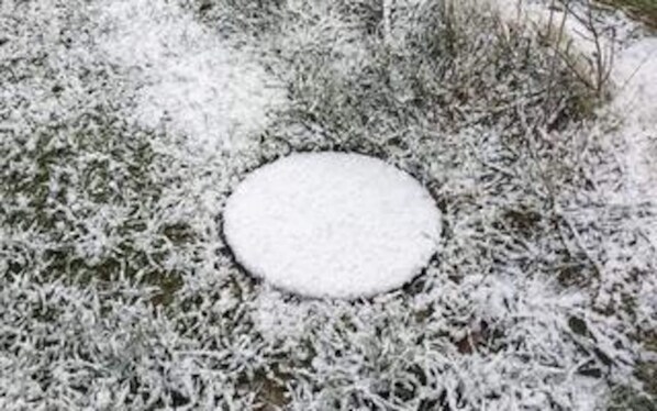 A snow-covered circular object on a grassy surface.