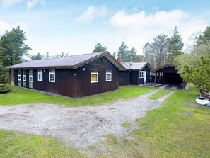 En toetages træhytte med grusvej og en overdækket veranda.
