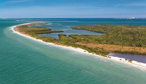 Luchtbeeld van een kustgebied met een zandstrand, helder turquoise water en weelderige groene begroeiing.