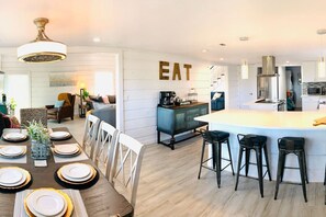 A modern kitchen with a central island, bar stools, and a dining area with a table set for four. - NEW! AUSTIN HILL COUNTRY CHARM! POOL/HOT TUB/VIEWS (Dripping Springs)