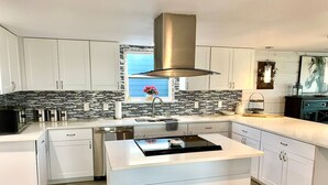 Una cocina moderna con armarios blancos, una isla central con estufa integrada y un amplio ventanal con vistas al exterior.