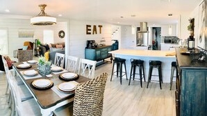 Una cocina moderna con una isla central, taburetes de bar y un comedor con una mesa larga para seis personas.