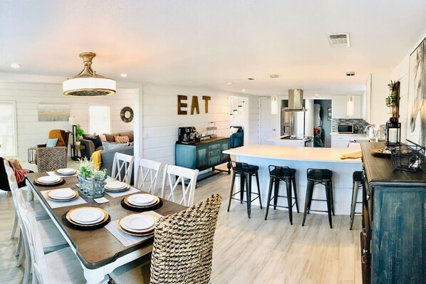 A modern kitchen with a central island, bar stools, and a dining area with a long table set for six.