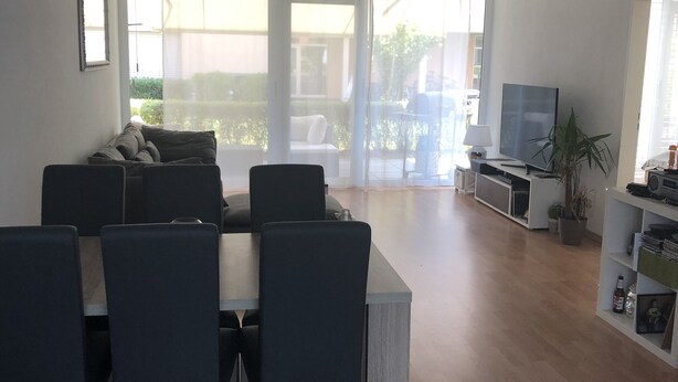 Ein modernes Wohnzimmer mit Essbereich, einem Flachbildfernseher und einer großen Schiebeglastür, die auf eine Terrasse im Freien führt.