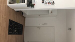 Ein modernes Badezimmer mit Holzboden, einem weißen Waschbecken und einem Spiegel. An der Wand befindet sich ein schwarzes Schild und auf dem Waschtisch ein kleiner Topf mit Pflanze.