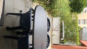 Ein Patio mit rundem Tisch und Stühlen, einem Metallzaun und einem Gebäude mit rotem Dach im Hintergrund.