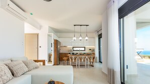 Sala de estar moderna com sofá, mesa de centro de madeira e cozinha ao fundo.