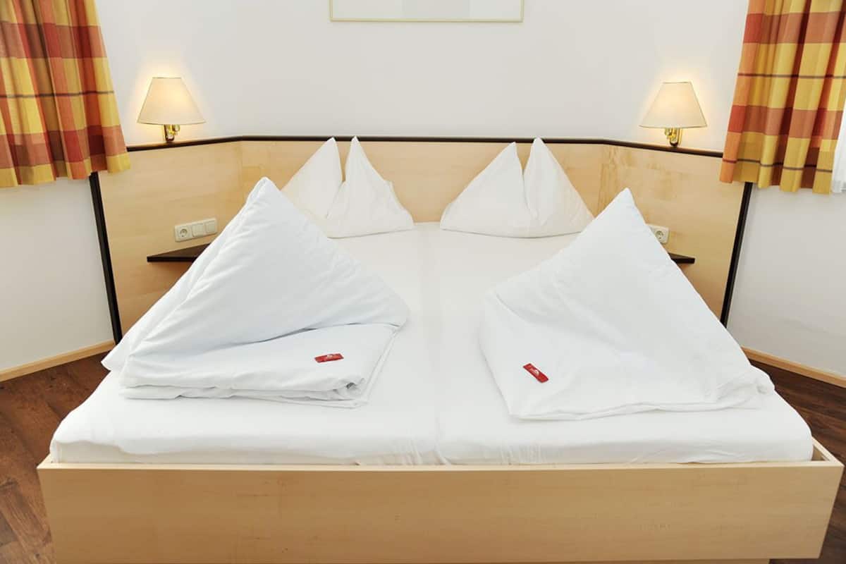 A neatly made bed with white linens and pillows, two bedside lamps, and a wooden headboard.
