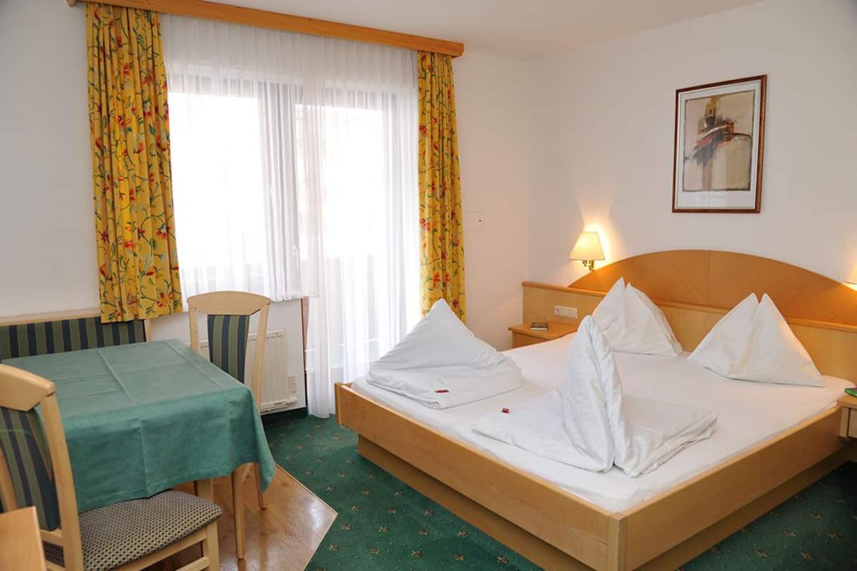 A hotel room with a bed, a table, chairs, a lamp, and a painting on the wall.