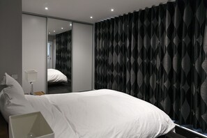 Experience a clean and functional space with a neatly made bed, bedside table, and large mirror.