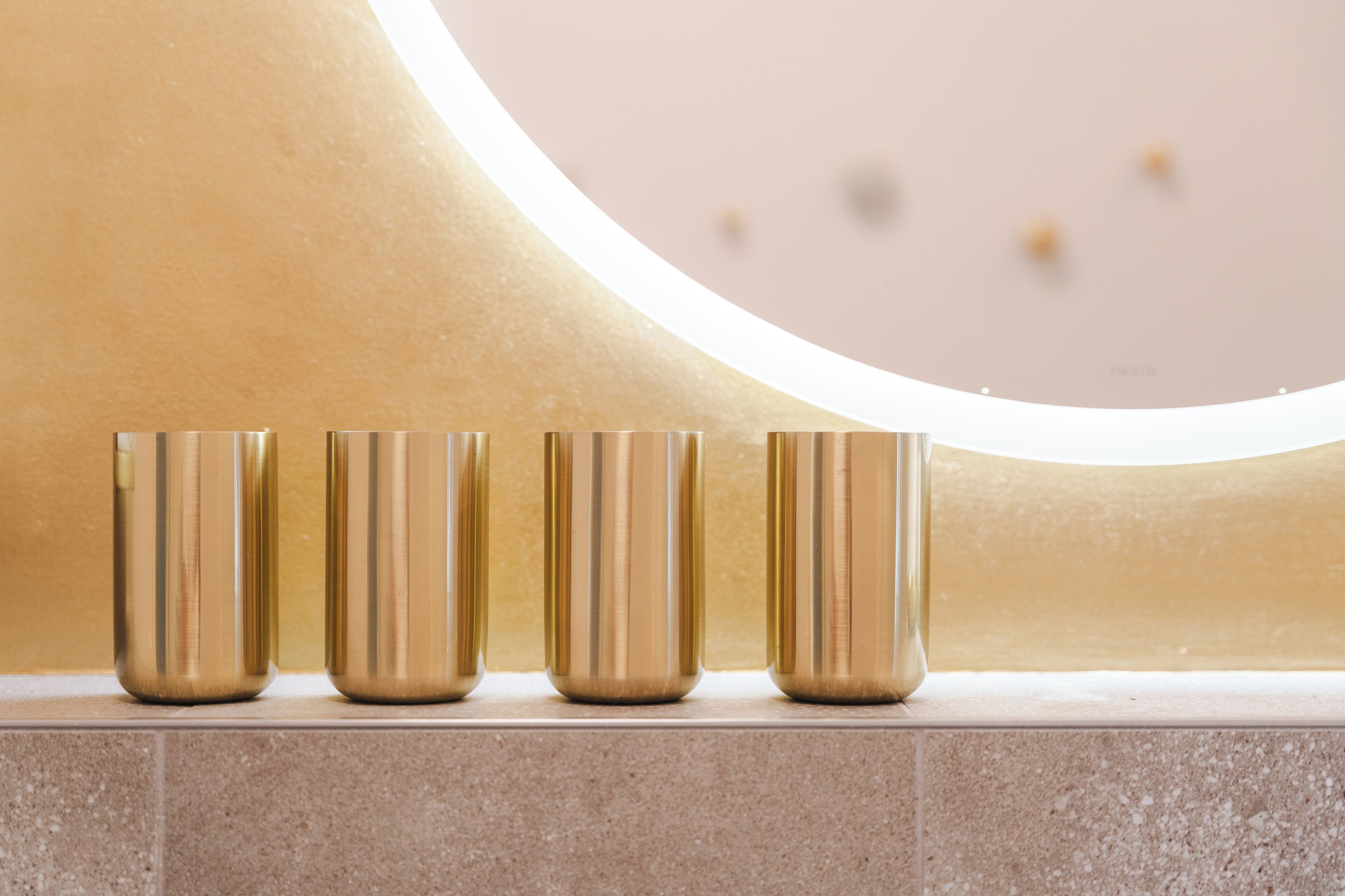 Four gold-colored cylindrical objects aligned on a tiled surface against a wall with a circular light fixture.