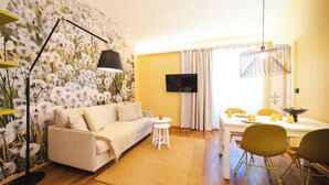 A living room with a sofa, a small round table, a floor lamp, and a dining area with chairs and a table. - GrazRentals (Graz)