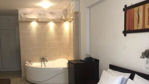 A hotel room with a large bed, a separate bathroom with a bathtub, and a small table with a lamp. - Melis Studios (Kassandra)