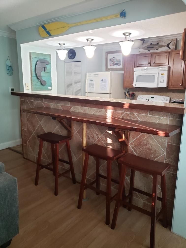 Cozinha com área de bar, banquetas de madeira, micro-ondas e um relógio na parede.