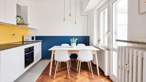 A modern kitchen with white cabinets, a yellow backsplash, a white dining table with two chairs, and a hanging light fixture. - Urban House Carducci - Attic (Turin)