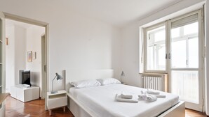 A modern bedroom with a large bed, bedside tables, a TV, and a window with blinds. - Urban House Carducci - Attic (Turin)