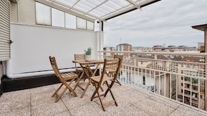 A balcony with a table and chairs, a potted plant, and a city view. - Urban House Carducci - Attic (Turin)