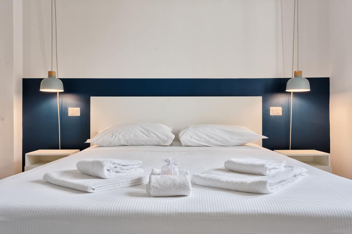 A neatly made bed with white linens and towels, two bedside tables with lamps, and a dark blue headboard.
