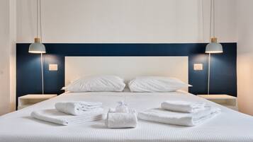 Ein ordentlich bezogenes Bett mit weißen Leinen und Handtüchern, zwei Nachttische mit Lampen sowie ein dunkelblaues Kopfteil.