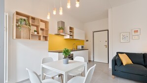Una cocina moderna con armarios blancos, una pared de acento amarilla y un comedor con mesa y sillas blancas.