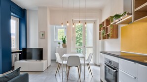 Una cocina moderna con armarios blancos, horno empotrado y comedor con mesa y sillas blancas.