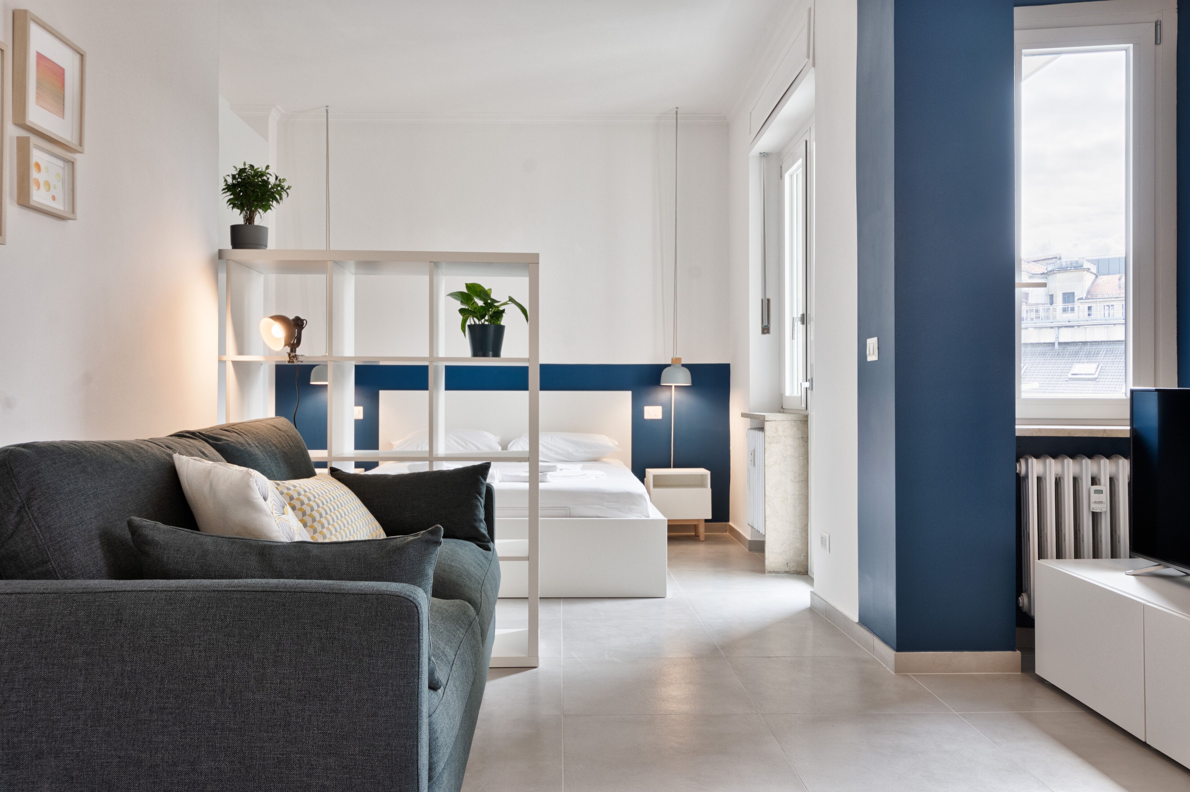 Ein modernes Wohnzimmer mit Sofa, Bett, Fernseher und einem Fenster mit Blick auf Gebäude.