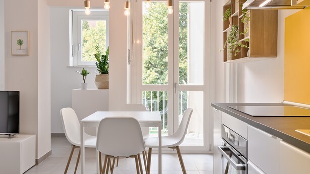 Una cocina moderna con armarios blancos, una mesa de comedor con sillas, un horno empotrado y un ventanal con vistas al verdor.