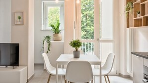 Una cocina moderna con armarios blancos, una mesa de comedor con cuatro sillas, luces colgantes y un televisor sobre un mueble.