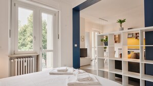 Habitación de hotel moderna con una cama grande, toallas blancas, un radiador, una pared azul de acento, un televisor y una estantería empotrada.