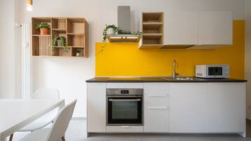 Una cucina moderna con mobili bianchi, una parete gialla a contrasto, forno integrato e microonde.