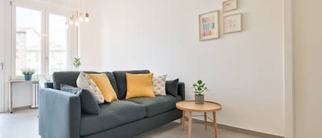 A modern living room with a grey sofa, wooden side table, and a small potted plant.