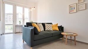 A modern living room with a grey sofa, yellow cushions, a wooden side table, and framed artwork on the wall. - Urban House Carducci - Apartments (Turin)