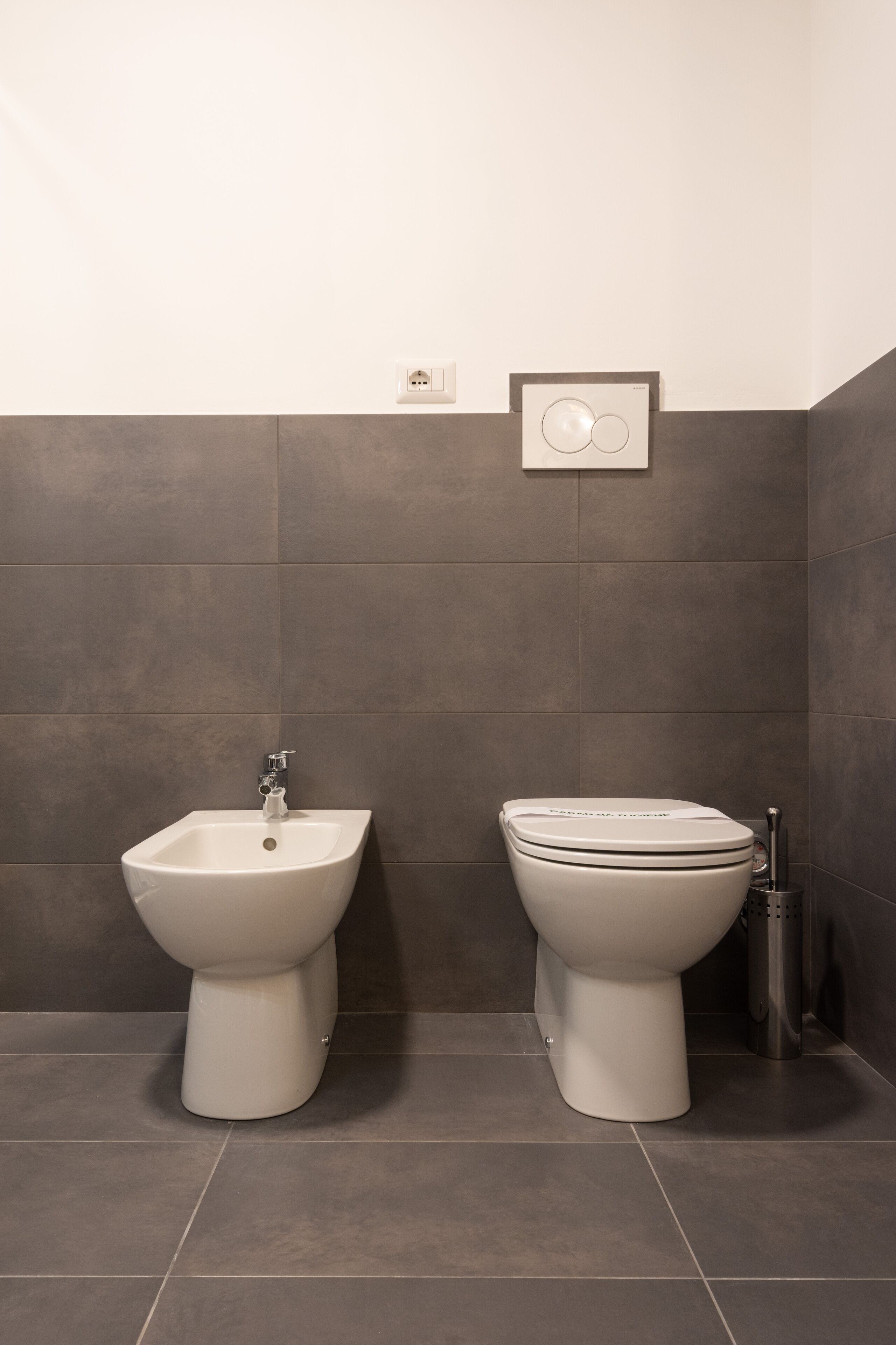 A bathroom with a bidet, toilet, and a wall-mounted electrical outlet.