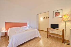 Habitación de hotel con una cama, un televisor sobre un soporte de madera, una lámpara y un cuadro en la pared.