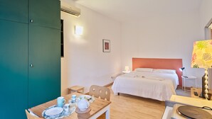 Et hotelværelse med en seng, et sengebord, en lampe og et spiseområde med et bord dækket til to personer.