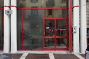 Una entrada de edificio con puerta roja, paneles de vidrio y una placa numérica.