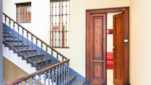 A staircase with a wooden handrail and metal balusters, leading to a room with a red sofa and a wooden door.