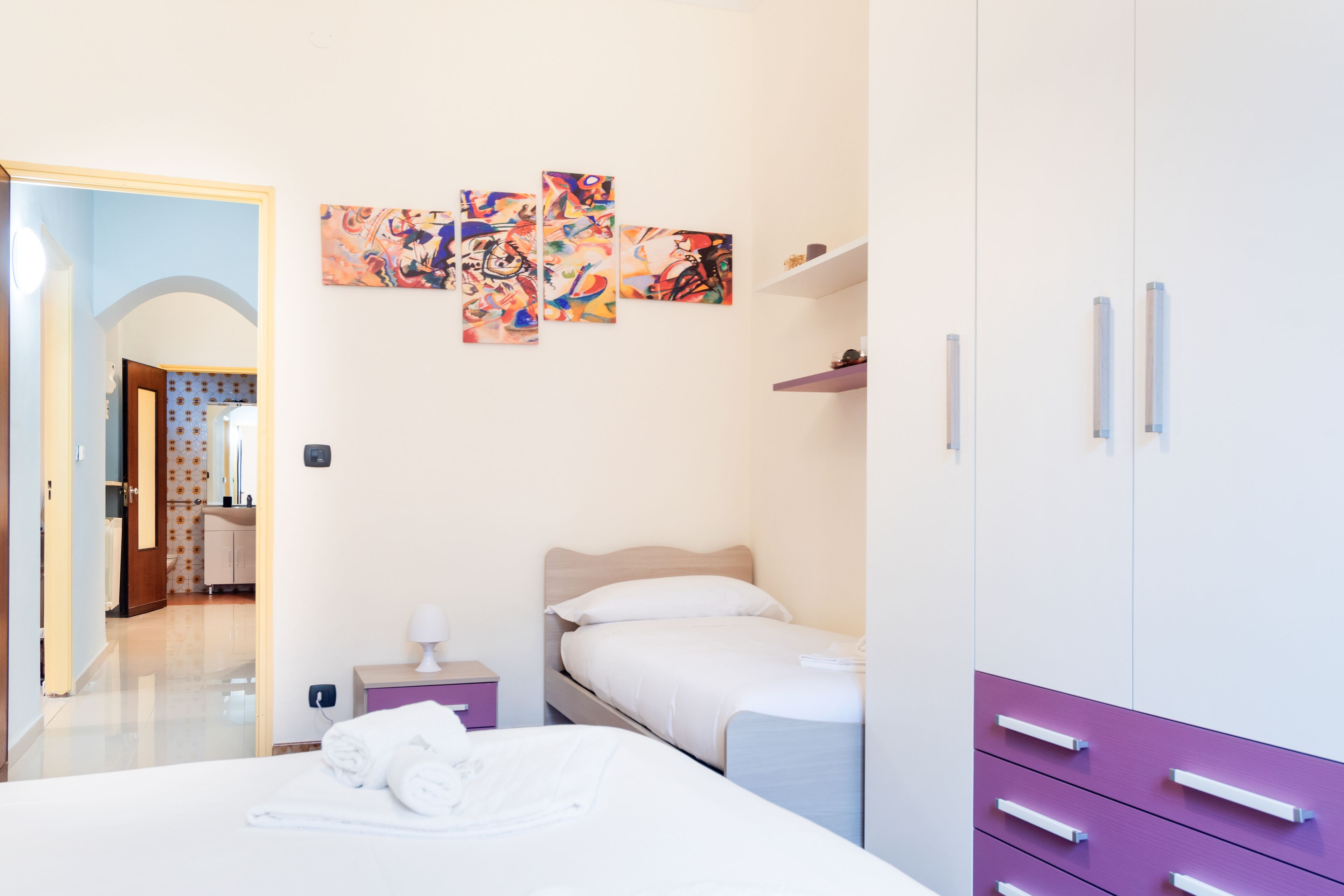 A hotel room with a bed, a bedside table, a wardrobe, and a wall with abstract art.