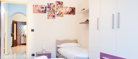 A hotel room with a bed, a bedside table, a wardrobe, and a wall with abstract art.
