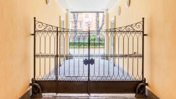 A wrought iron gate with a star design, leading to a building with a balcony and a view of trees and buildings in the background.