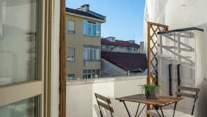 Ein Balkon mit Tisch und Stühlen, einem Blumentopf und Blick auf benachbarte Gebäude.