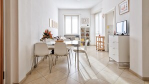 Ein moderner, gut beleuchteter Essbereich mit einem weißen Tisch, vier Stühlen und einem Fernseher auf einem Schrank.