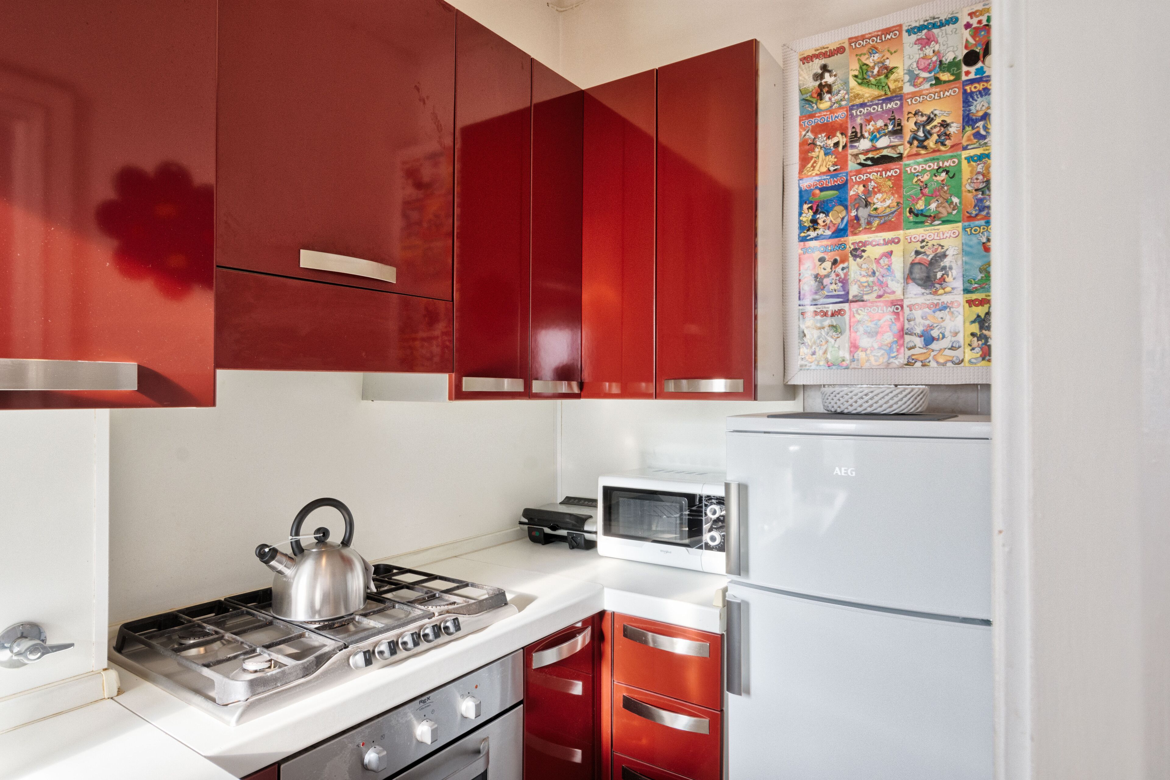 A kitchen with red cabinets, a white countertop, a gas stove, a microwave, and a white refrigerator.
