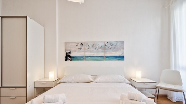 Ein Hotelzimmer mit einem großen Bett, zwei Nachttischen, einem Sessel und einem Wandbild von fliegenden Vögeln über dem Meer.