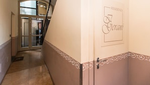 Um corredor com uma porta identificada como "RESIDENZA Gerani" e uma escadaria que leva a outro andar.