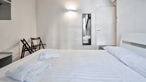 Ein Hotelzimmer mit einem ordentlich bezogenem Bett, einem Sessel, einem Nachttisch und einem Spiegel.