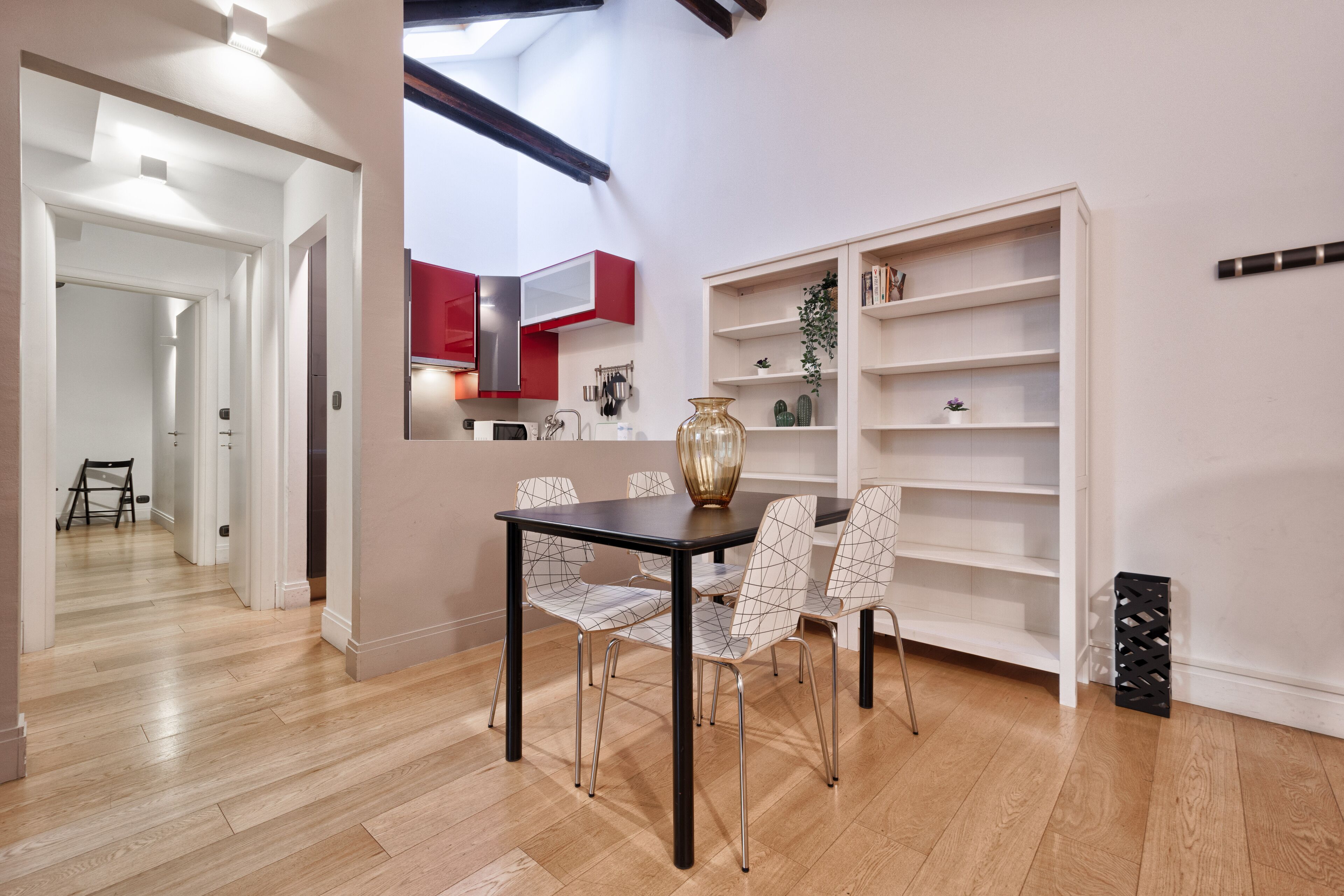 Un comedor con una mesa y sillas, una estantería y una cocina al fondo.