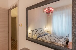 Un dormitorio con un espejo grande, una cama con cubrecama estampado, una araña y una puerta que da a otra habitación.
